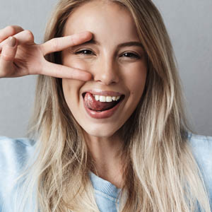 A woman holds up a sideways peace signs next to her eye as she thinks about the services at Lovett Dental Vintage Park