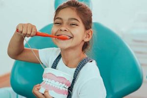 A little girl smiles as she brushes her teeth, showing what she learned using pediatric dentistry in Kohrville, TX