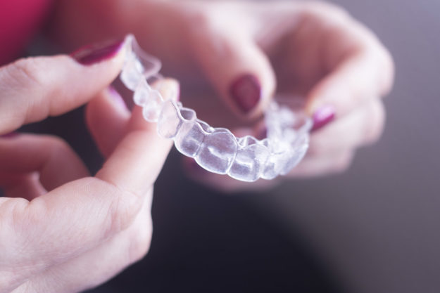 how to prevent teeth shifting (1) woman picking up a retainer to prevent teeth shifting