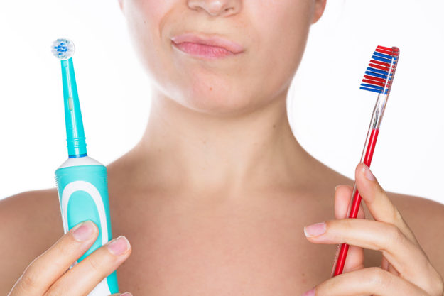 types of toothbrushes (1) woman contemplating two types of toothbrushes