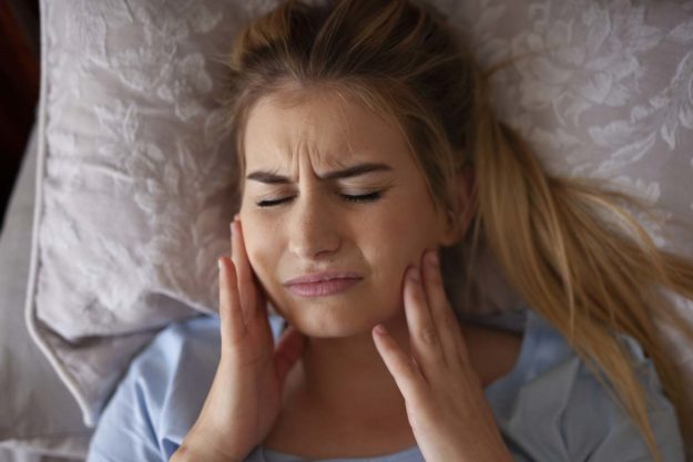 bruxism-treatment young girl in bed holding jaw needing bruxism treatment options
